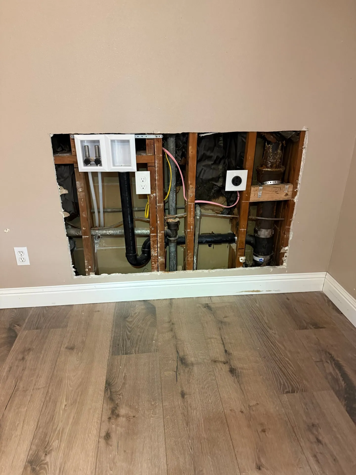Wall opened in a downstairs unit in Vancouver WA showing the new washer and dryer rough-in boxes set between studs before the drywall patch