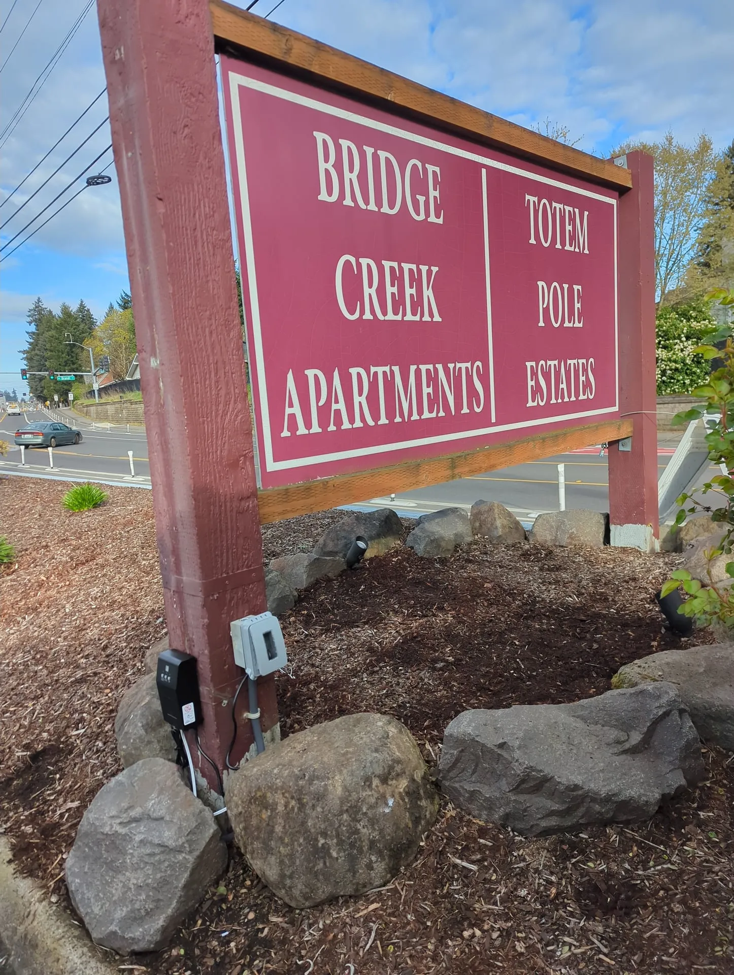 Small weatherproof enclosure mounted low on the timber post of a monument sign in Vancouver WA, housing the low-voltage transformer and controls for the sign lighting