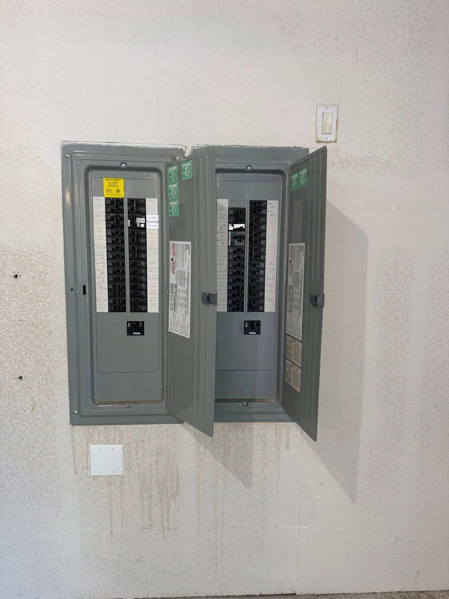 Main panel and sub panel side by side on a wall in a Vancouver WA home, both opened with dead fronts removed, showing where the three new circuits were landed