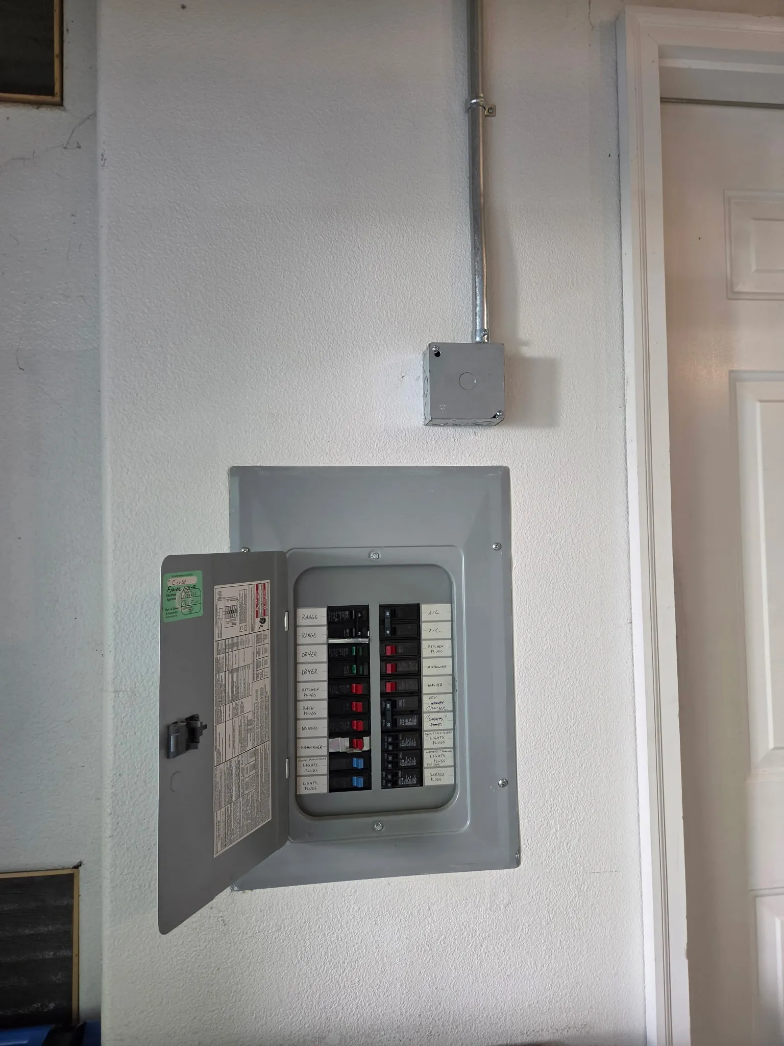 Residential electrical panel with its door open in a Vancouver WA garage, a new EMT conduit leaving the top of the panel to a junction box on its way to the EV charger