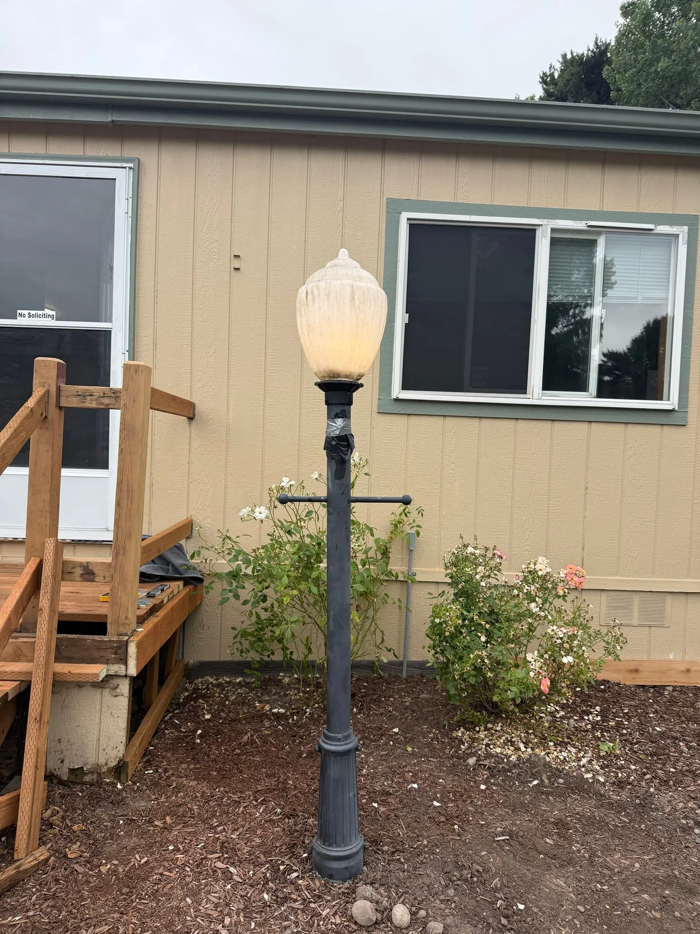 Restored cast post lamp lit at dusk beside a garden path at an Orchards home in Vancouver WA, with the deck and house behind it