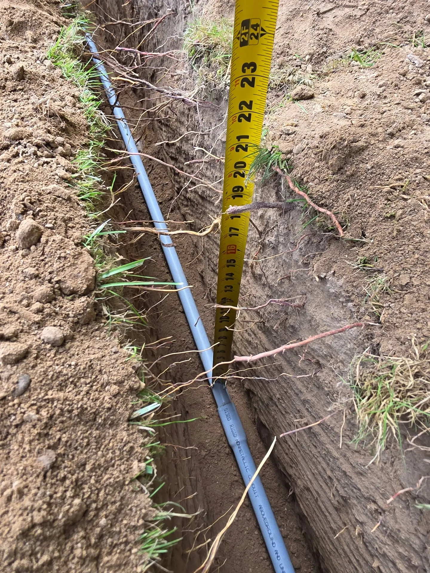 Gray PVC conduit in the bottom of a trench with a yellow tape measure showing the depth at a Kelso WA home