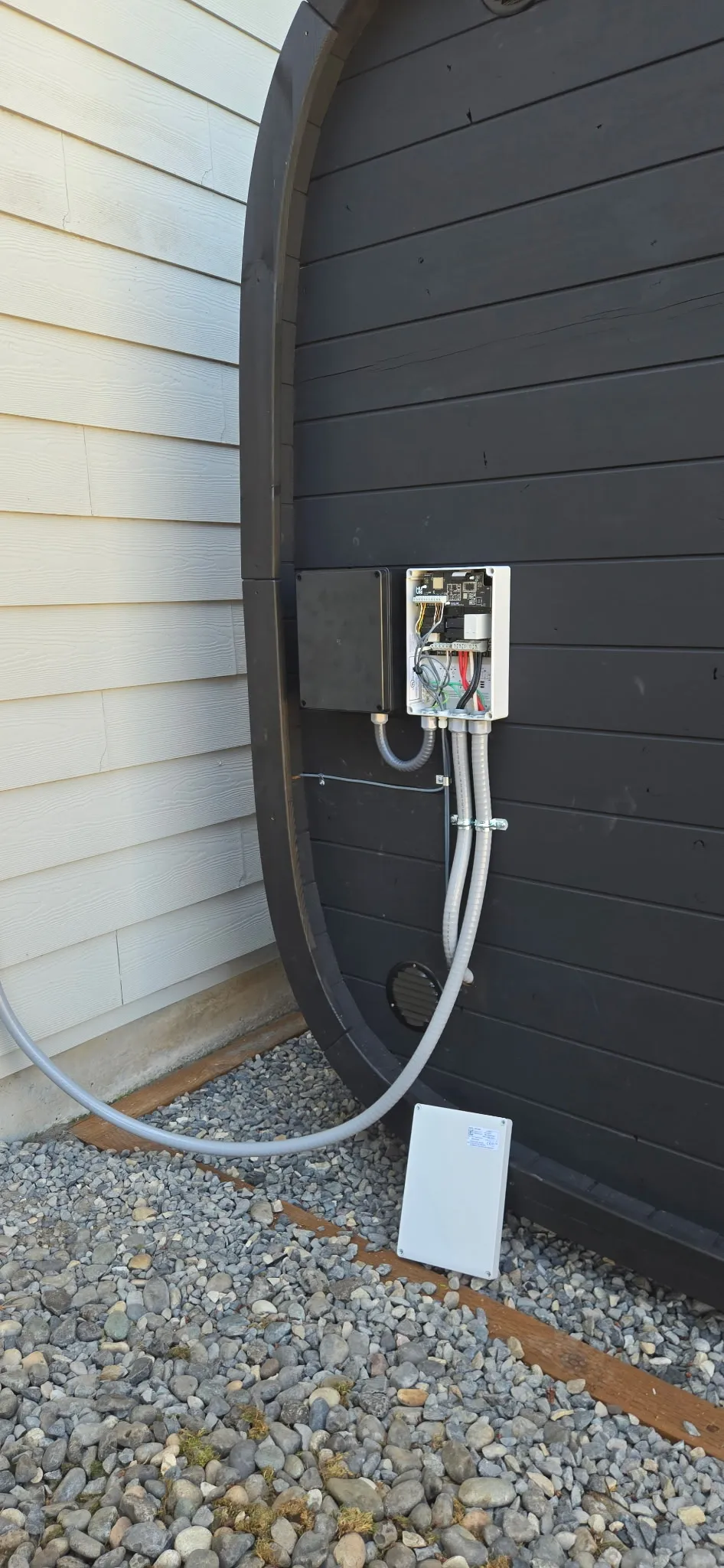 Electrical disconnect box mounted on the exterior wall of an outdoor sauna in Washougal WA with flexible whip and conduit running down to the gravel bed