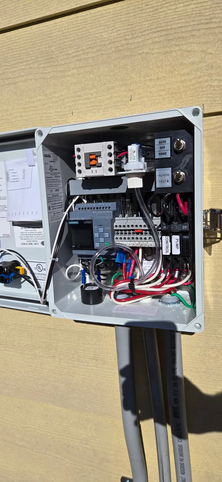 Interior of an open SunWater septic control panel in Kalama WA showing a Siemens LOGO controller, contactor, terminal blocks, and separate control and pump breakers with AUTO OFF HAND and alarm test switches
