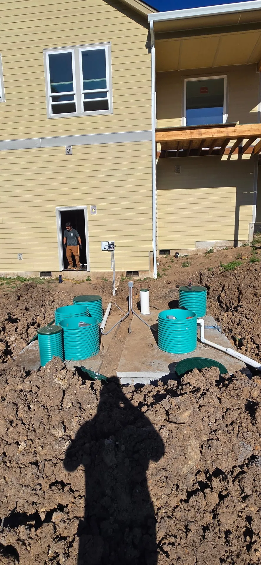 Two green septic tank risers set in a graded yard behind a new-construction home in Kalama WA with the conduit trench running back toward the house