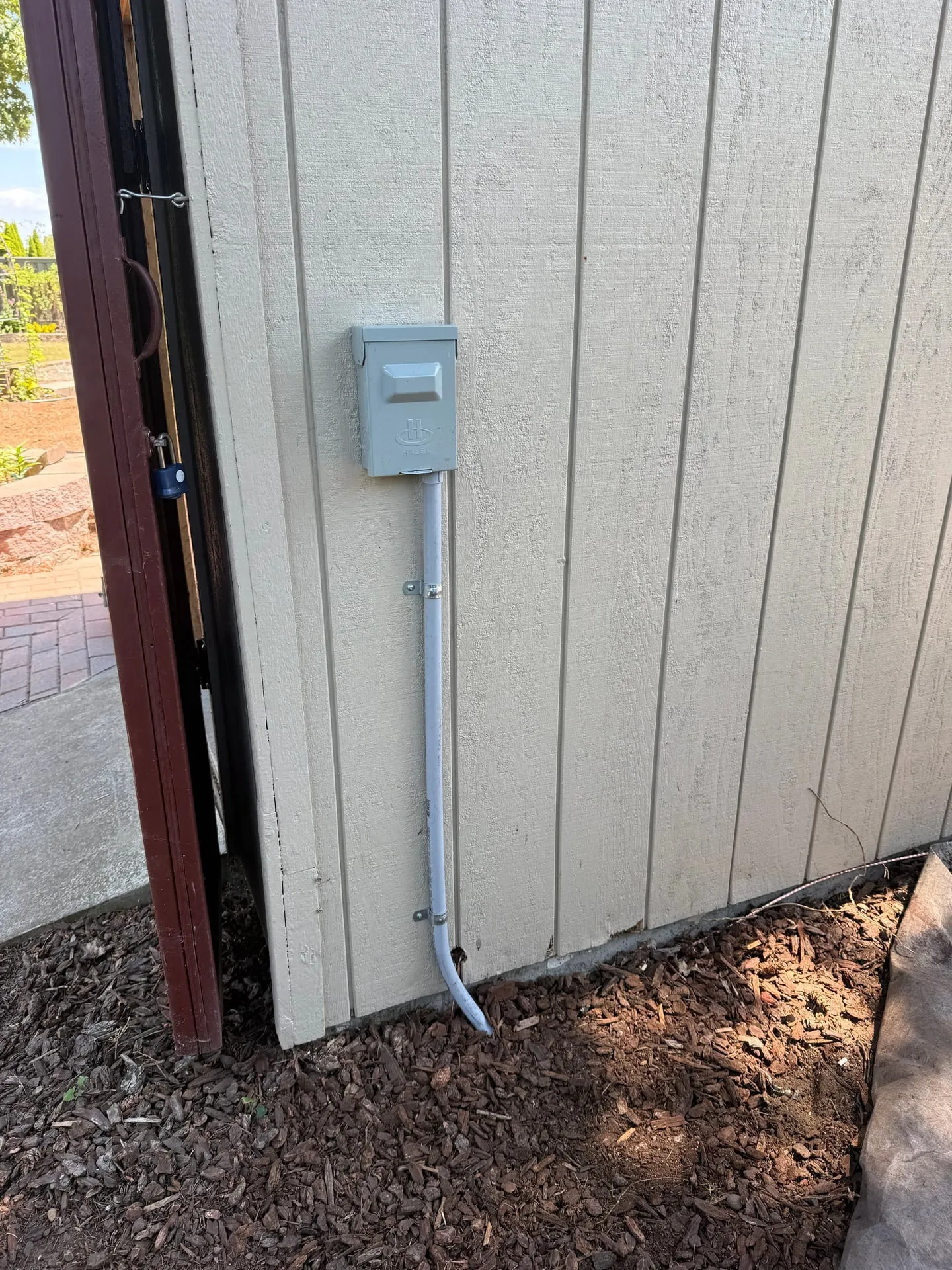 Exterior wall of a backyard shed in Vancouver WA with a new weatherproof electrical enclosure mounted on the siding and conduit dropping to grade