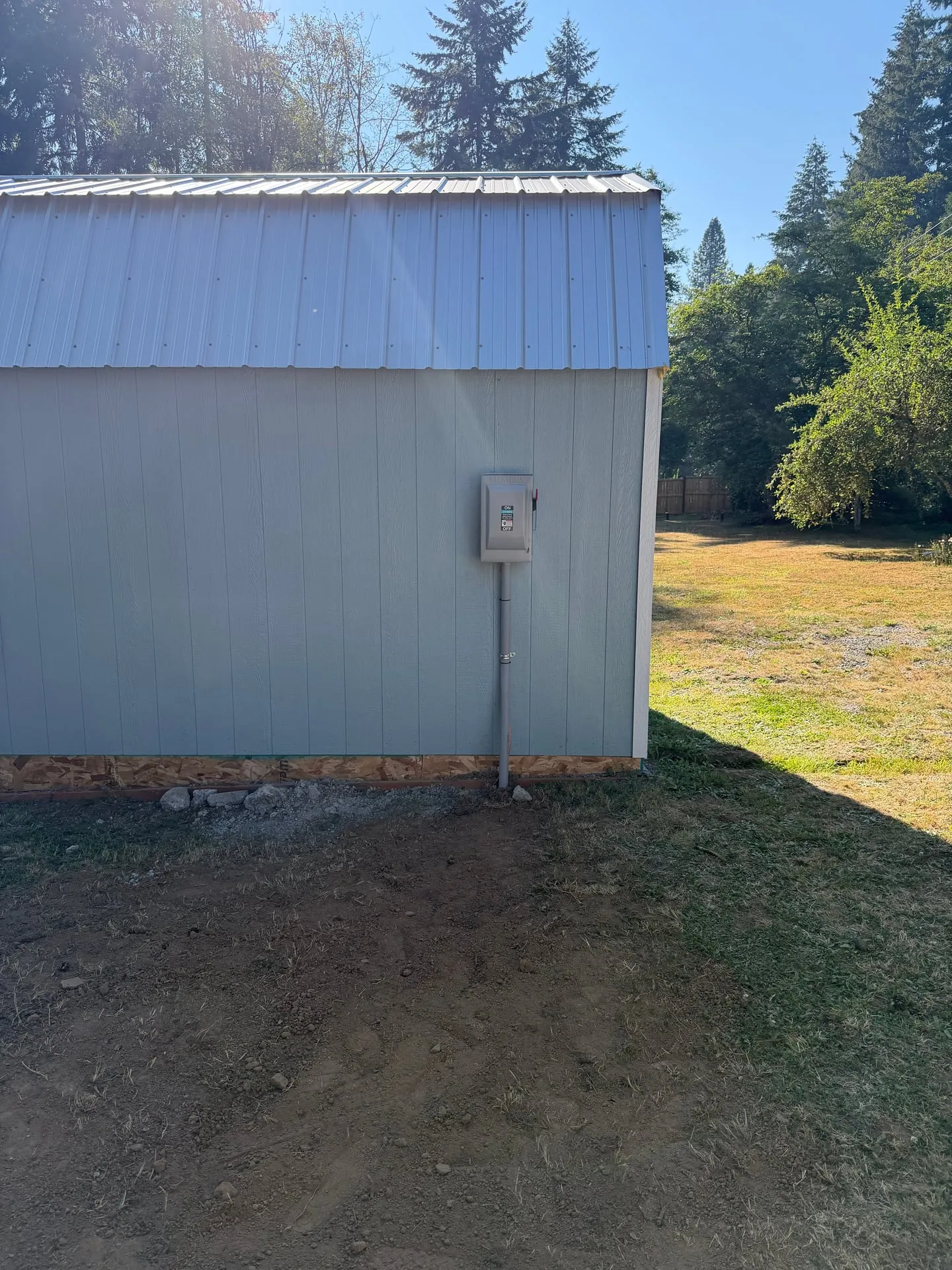 Blue metal shed on a rural Woodland WA property with a new electrical enclosure mounted on the exterior wall and freshly graded soil along the base