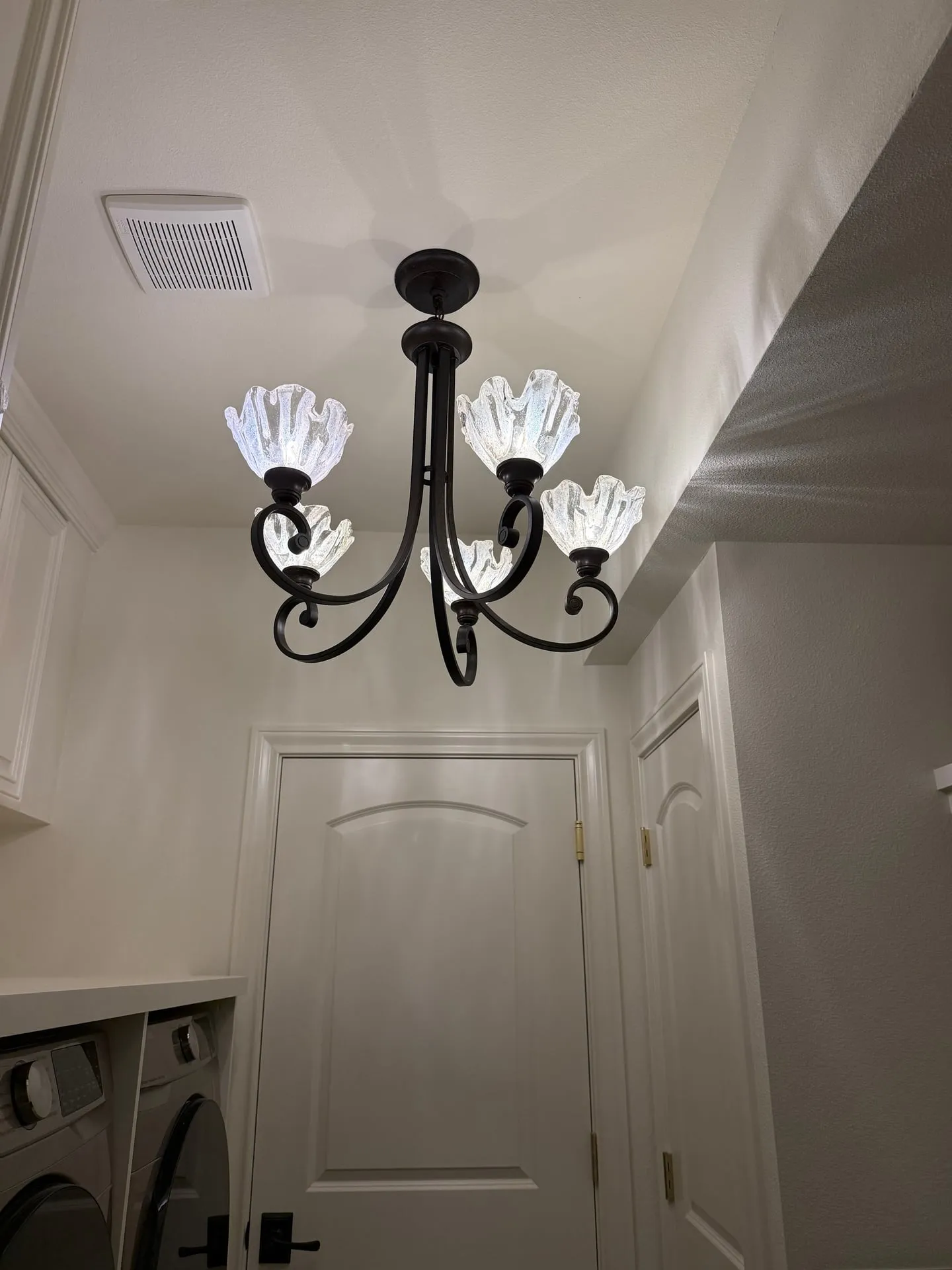 Black and glass chandelier hanging in the stairwell of a custom home in Ridgefield WA above a panelled white wall and dark interior door