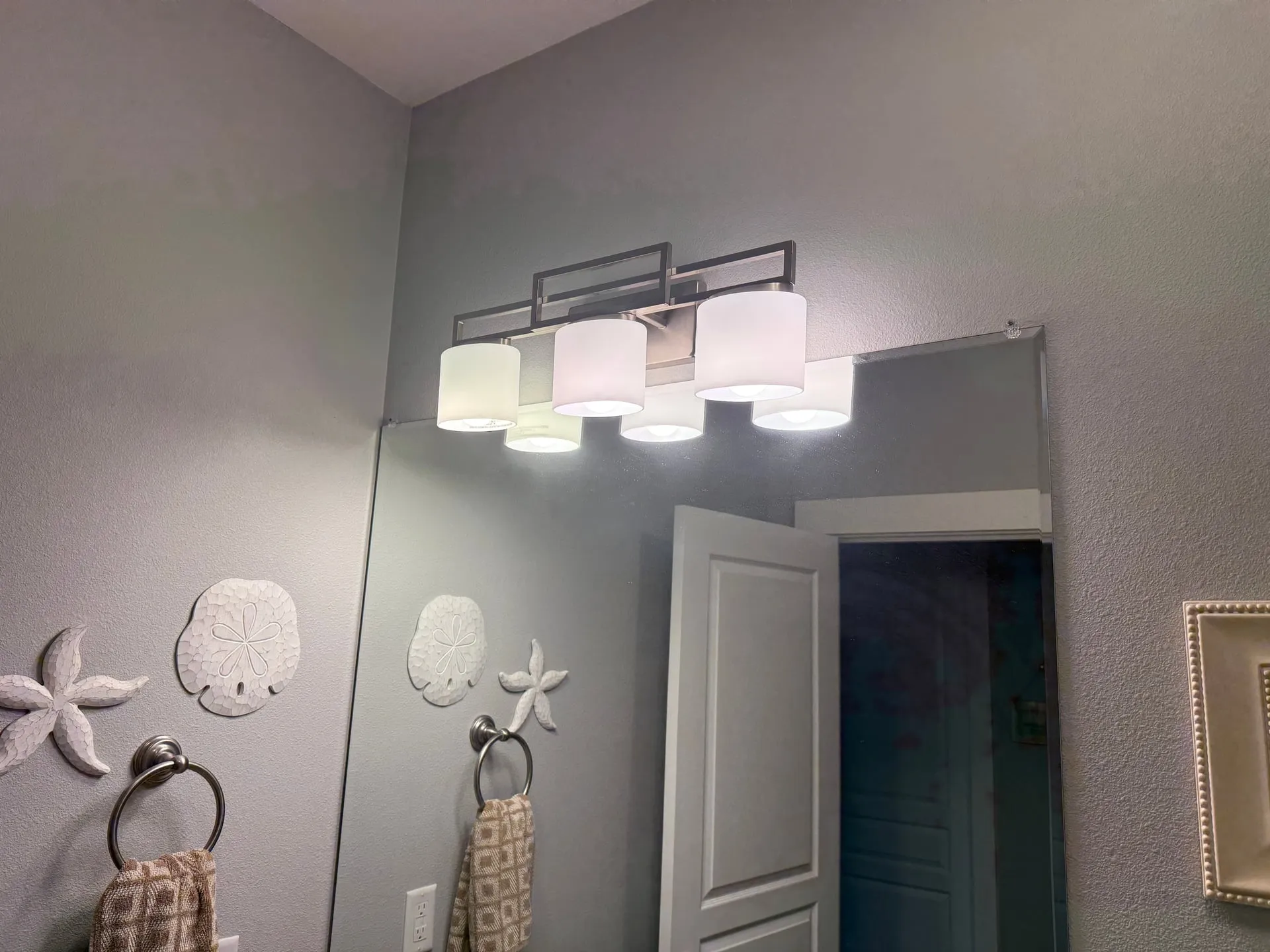 New three-light vanity fixture with frosted glass shades installed above the mirror in a Ridgefield WA bathroom, lit and reflecting off the grey wall