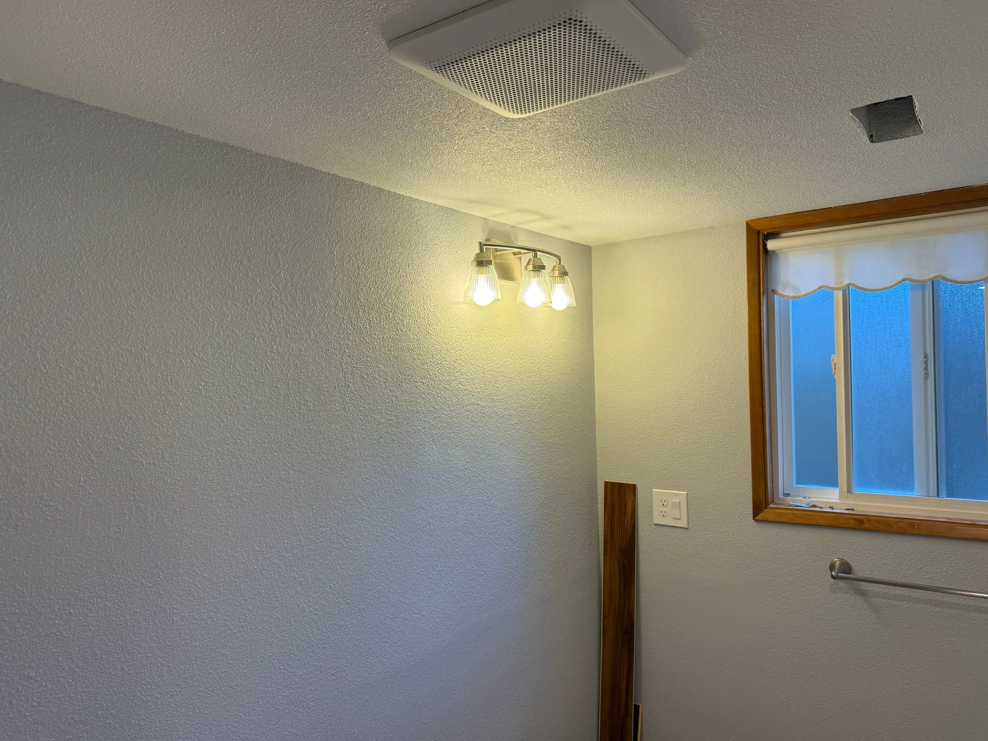 Close view of a lit three-bulb vanity light and the Panasonic exhaust fan grille in a remodeled bathroom in Felida, Vancouver WA