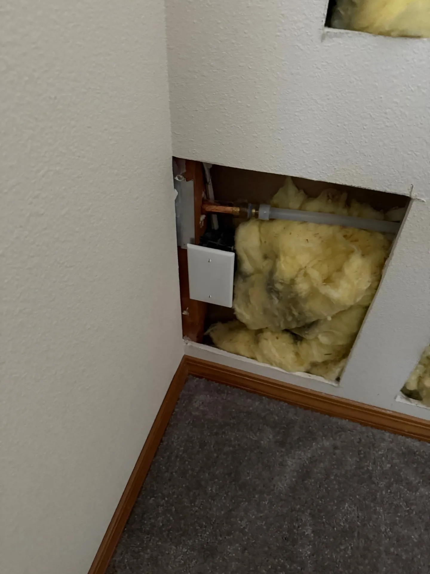 Section of drywall cut out near the floor in an east Vancouver WA bedroom, showing insulation and copper pipes inside the wall